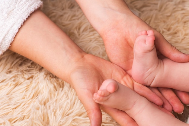 Mom holds in her hands a small baby foots. Small legs of a newborn baby in the hands of mother. Baby foot massage. Maternal love and care