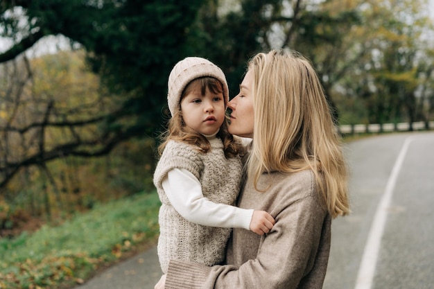 Mom holds her little daughter in her arms and they walk in warm sweaters on an autumn day