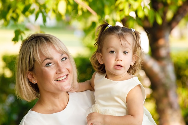 Mom holds little daughter in her arms in the park in summer in sunny weather