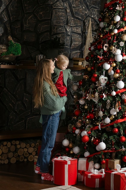 Mom holds little girl on her arms near Christmas tree Christmas tree at home New Year mood Mother and daughter decorate Vertical frame