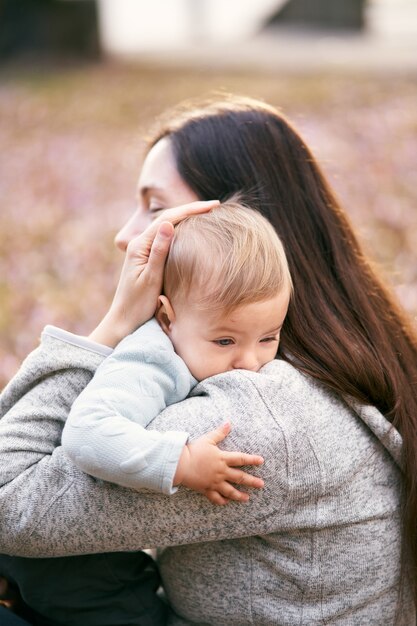 Mom hugs the baby to her chest sitting on the foliage in the park closeup