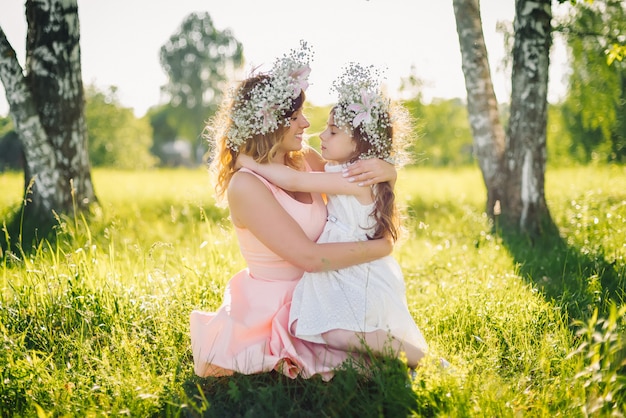 Mom hugs her daughter sitting on the grass outdoors on a Sunny summer