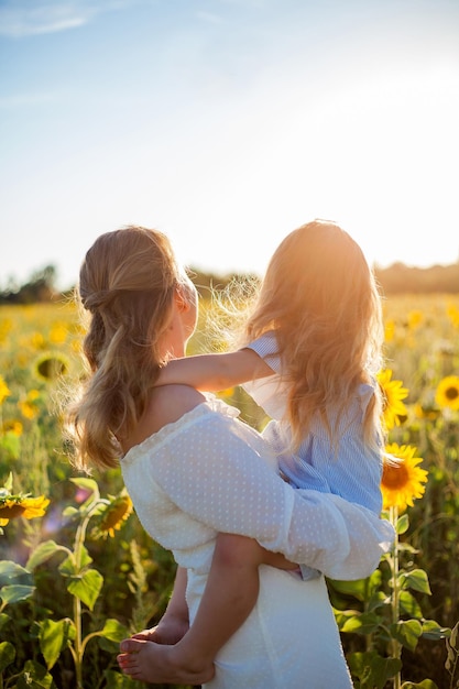 Mom hugs her little daughter A beautiful young woman with a 4yearold child in her arms in a sunflower field Summer