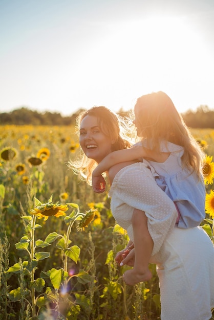 Mom hugs her little daughter A beautiful young woman with a 4yearold child in her arms in a sunflower field Summer