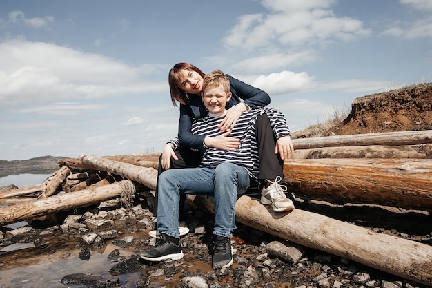 Mom hugs her son on the riverbank. A beautiful, modern mother with a happy son in striped vests.