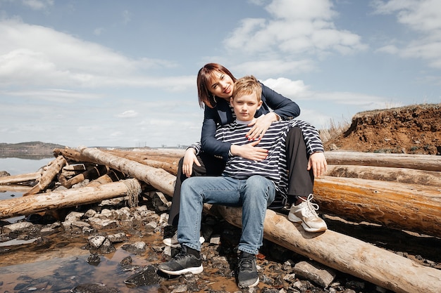 Photo mom hugs her son on the riverbank. a beautiful, modern mother with a happy son in striped vests.