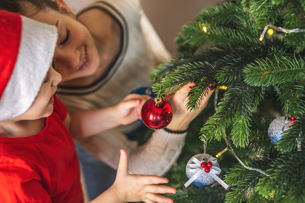 写真 ママは彼女の子供の息子がクリスマスツリーを飾るのを手伝っています