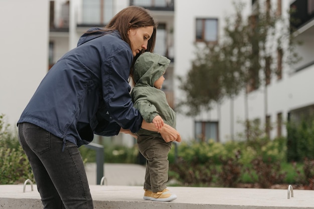 A mom is teaching her female toddler how to do steps in the street at noon