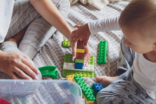 Mom and kid play together in the bedroom on a bed with plastic blocks