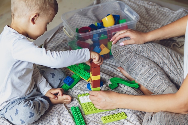 Mamma e bambino giocano insieme in camera da letto su un letto con blocchi di plastica