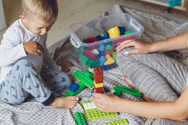 Mom and kid play together in the bedroom on a bed with plastic blocks