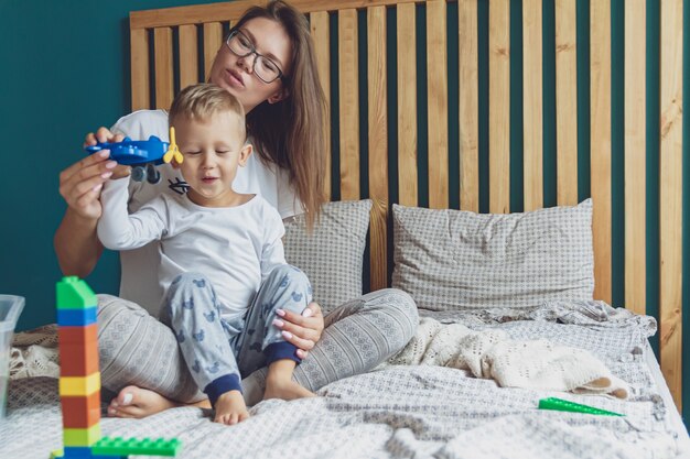 Photo mom and kid play together in the bedroom with plastic blocks