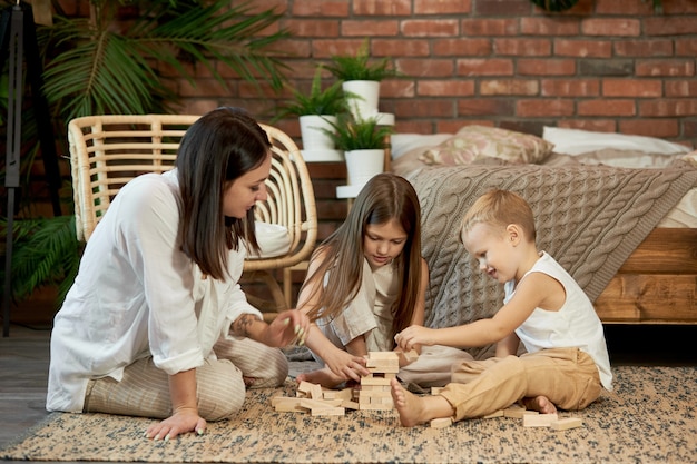 Mom and kids play squirl tower. Woman girl and boy play family puzzle game. Family day off