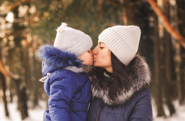 Mom kisses a little girl on a walk in the woods in winter. Motherly love