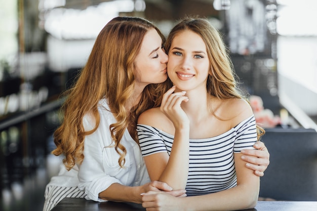Фото Мама целует дочь-подростка на летней террасе кафе в повседневной одежде