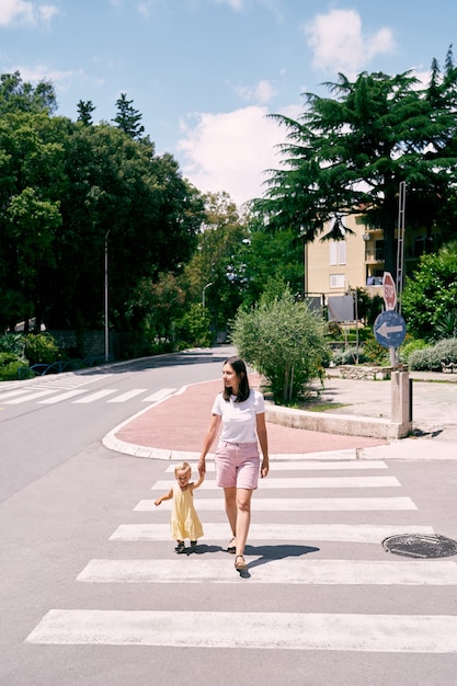 Mom leads the girl along the zebra crossing across the road