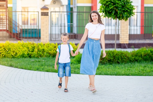 La mamma conduce il figlio di suo figlio per mano con uno zaino a scuola o all'asilo e torna a scuola