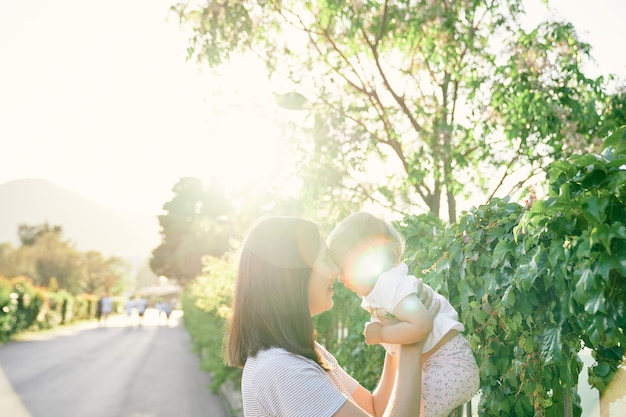 写真 ママはツタと絡み合った柵で小さな女の子を腕に抱き上げた