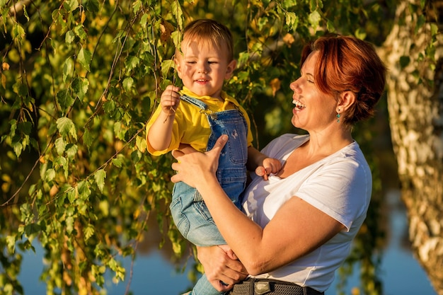 Mamma e ragazzino si siedono sulla riva del fiume sotto i raggi del sole al tramonto in una sera d'autunno