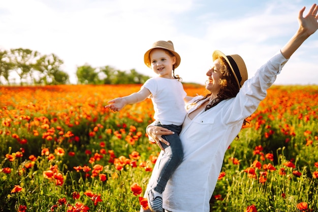 Mom and little daughter are playing in the field of flowering poppies