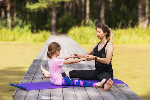 Mom and little daughter do stretching exercises on a sunny summer morning in nature