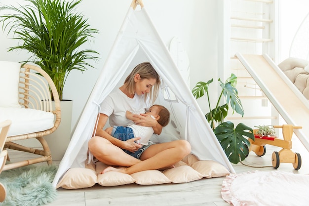 Mom lulls little baby daughter while sitting in a hut in the playroom