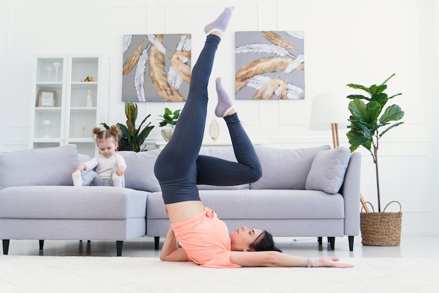 Mom making stretching exercises with baby girl at home.