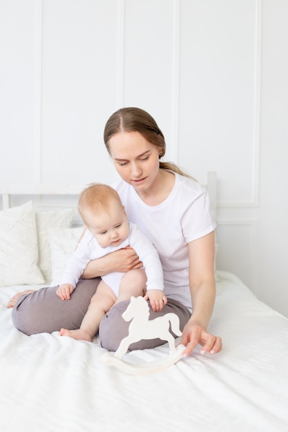 Mom plays with baby wooden toy horse on the bed at home, happy family