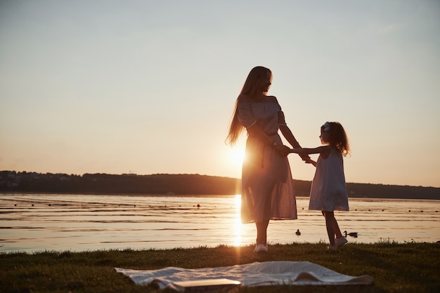 お母さんは、夕暮れ時のシルエット、海の近くの休日に彼女の赤ちゃんと遊ぶ