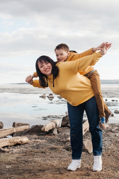 Photo mom plays with her son on the riverbank. a beautiful mother and son in yellow hoodies are having fun playing and smiling on a sunny day. outdoor recreation.