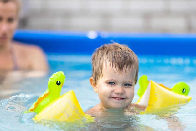 Mom plays with a naked baby in oversleeves in the pool against the background of a summer sunset