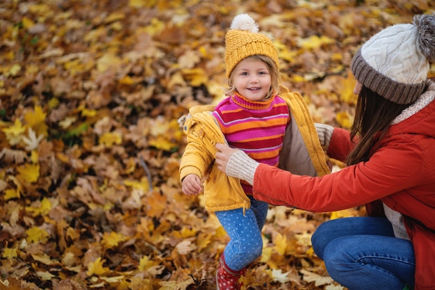 Mom puts on her little daughter's jacket in the autumn forest