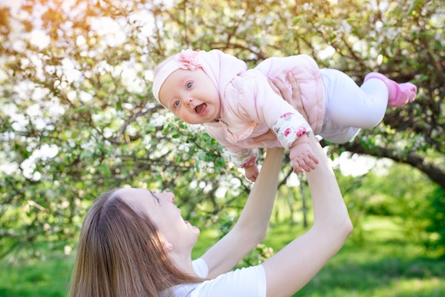 Mom raised his daughter in his hands on nature background. Baby is fly. Happy motherhood.