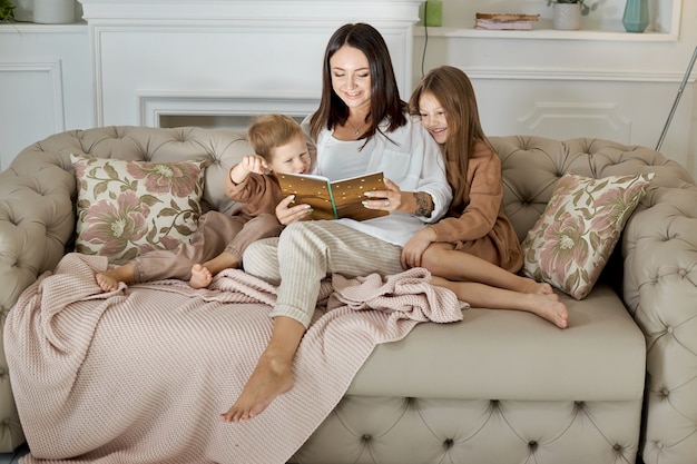 Mom reads a book to the children. A woman tells a story to a boy and a girl before going to bed. Mom daughter and son relax at home on a day off