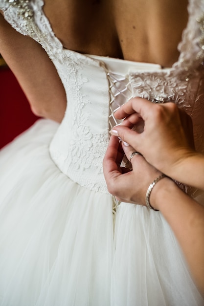 Le mani della mamma legano il corsetto dell'abito da sposa della sposa