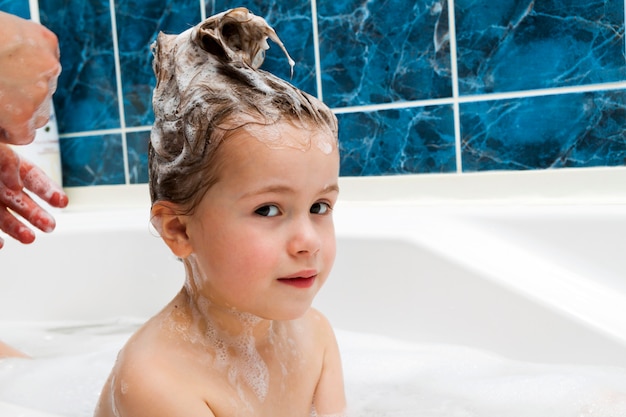 Le mani della mamma lavano la testa della piccola ragazza in bagno.