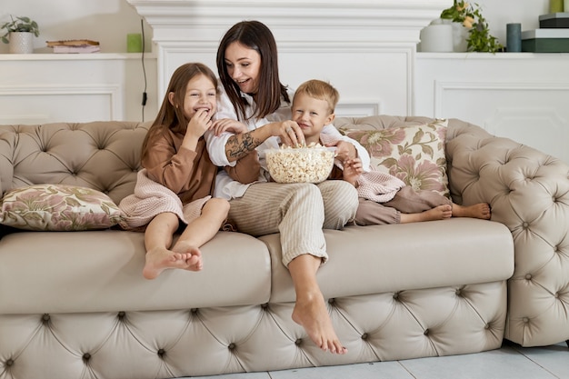 Mom sits on the couch with her son and daughter and watch a movie