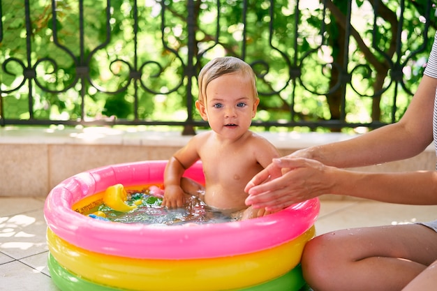 La mamma si siede sul pavimento accanto a un bambino in una piccola piscina gonfiabile