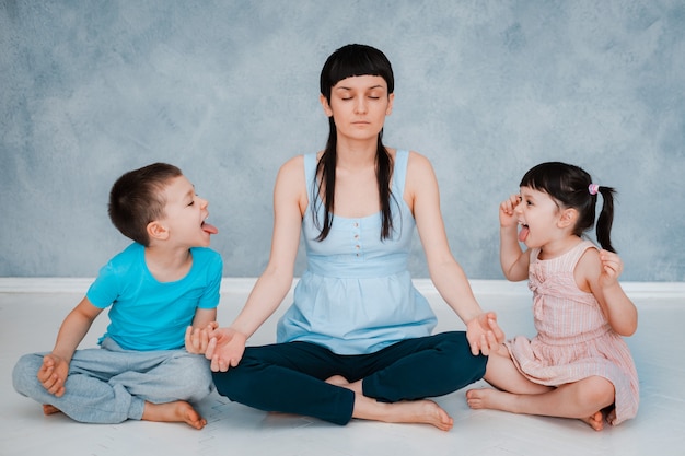 Mom sitting floor, meditating Lotus position, small children are screaming playing around focused calm mom meditating balancing