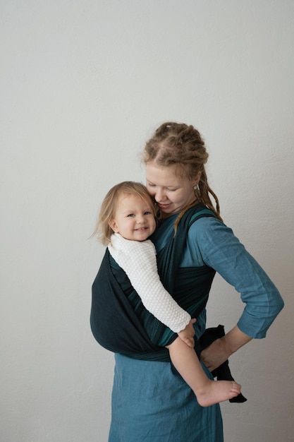 Mom in a sling with a happy daughter for the convenience of motherhood and taking care of the child