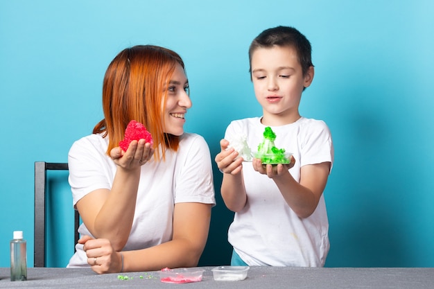 Mom and son are holding grown red and green crystals on a blue surface.