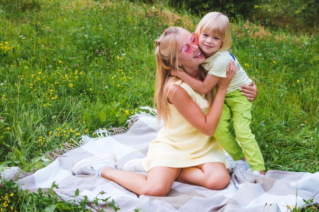 Mom and son are hugging on a blanket in the park. Close-up portrait. Woman in pink sunglasses