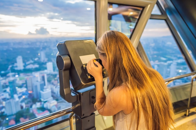 Mom and son are looking at Kuala lumpur cityscape Use binoculars Panoramic view of Kuala Lumpur city skyline evening at sunset skyscrapers building in Malaysia Traveling with kids concept