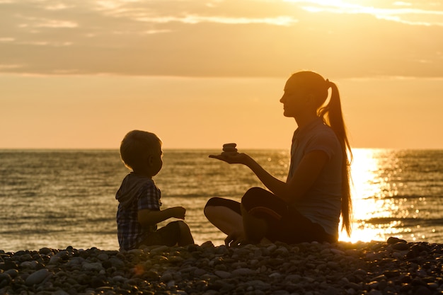 ママと息子は夕暮れ時のビーチで遊んでいます。