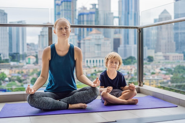 Mom and son are practicing yoga on the balcony in the background of a big city sports mom with kid