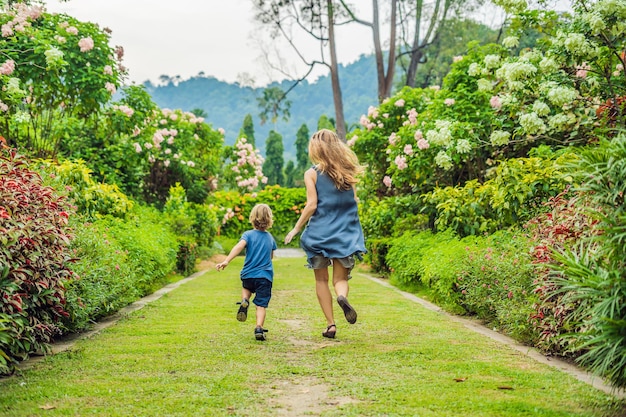 엄마와 아들은 꽃이 만발한 정원에서 뛰어 다니고 있습니다. 행복한 가족 생활 스타일 개념입니다.