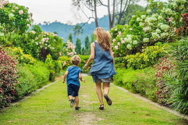 엄마와 아들은 꽃이 만발한 정원 행복한 가족 생활 스타일 개념에서 뛰어 다니고 있습니다