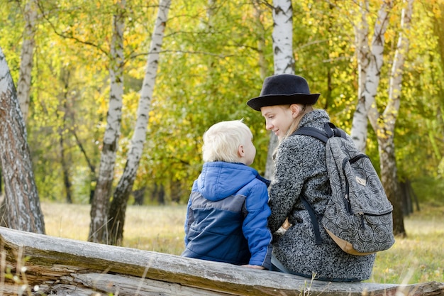 Mom and son are sitting in the autumn forest on a log. Back view