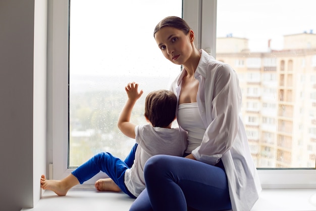 Mom and son are sitting in a white shirt and a t-shirt by window