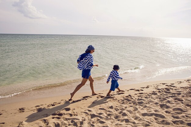 Мама и сын в синей одежде бегут к морю на пляж летом во время отпуска